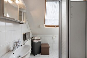 A bathroom with a sink, mirror, window, and a small storage box.