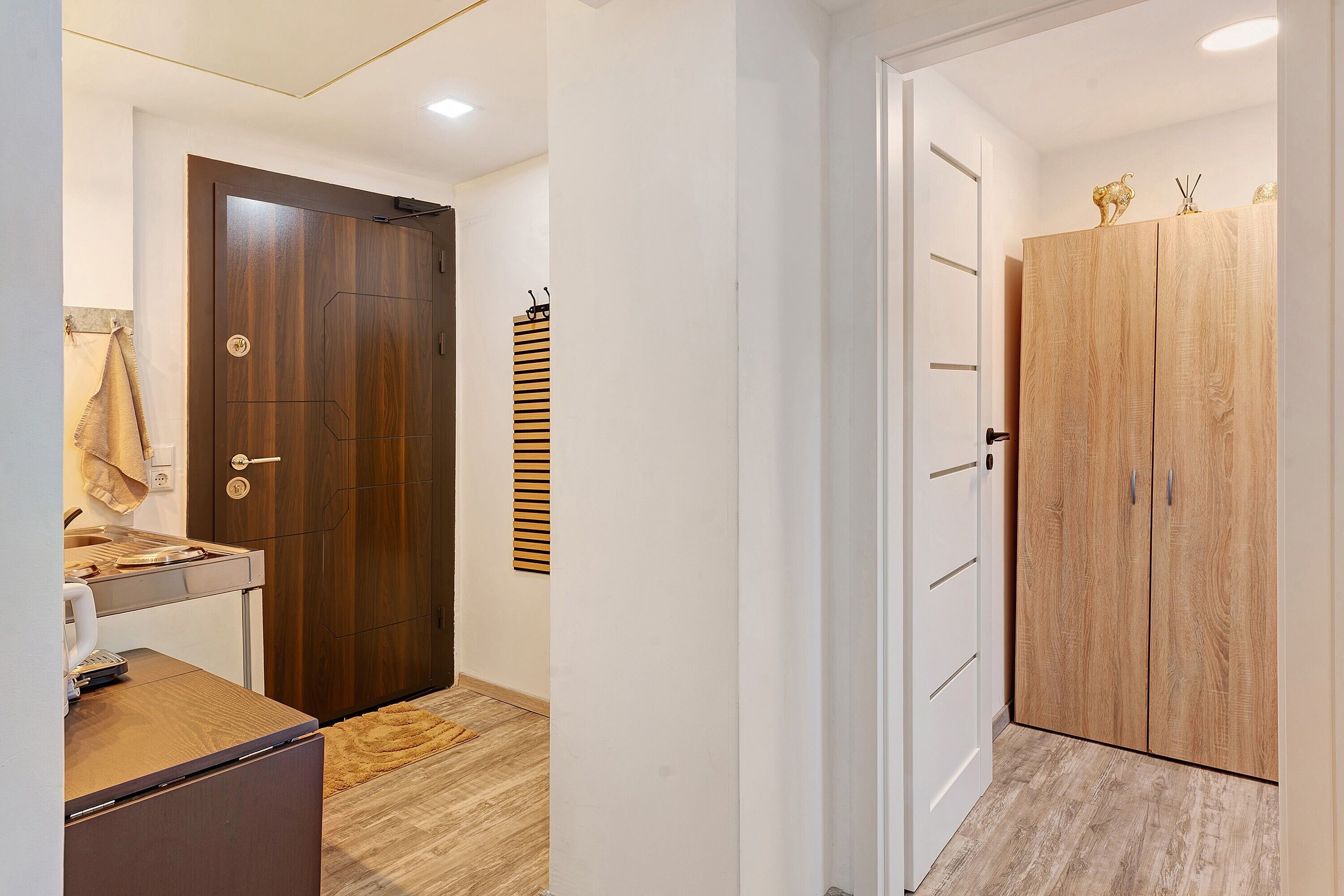 Un couloir avec une armoire en bois, une petite table sur laquelle se trouve une bouilloire, et une serviette accrochée au mur.
