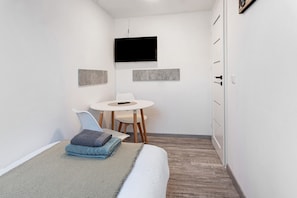 Una habitación pequeña y moderna con una cama, un escritorio y un televisor.