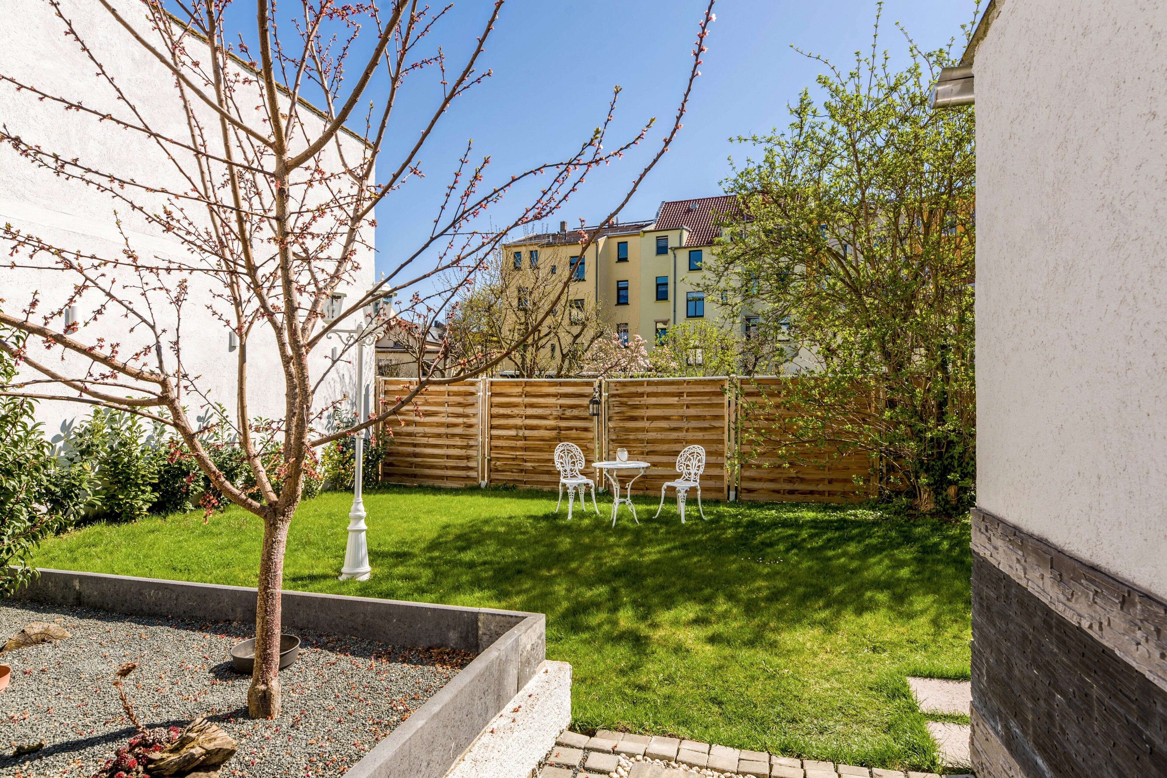 A courtyard with a small garden, a fire pit, and two white chairs.
