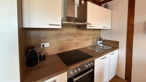 A compact kitchen with white cabinets, a stainless steel range hood, a built-in oven, and a sink. - Room 'Müller Thurgau' with Private Balcony, Wi-Fi / Including Breakfast (Endingen am Kaiserstuhl)