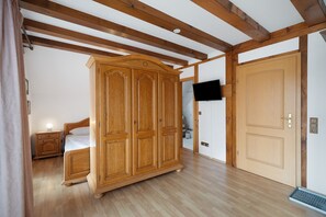 Une chambre à coucher avec une armoire en bois, un lit, une table de chevet, un téléviseur fixé au mur et une porte.
