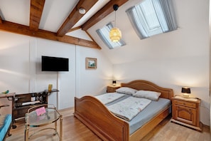 A bedroom with a wooden bed, a desk with a chair, a TV mounted on the wall, and a skylight.