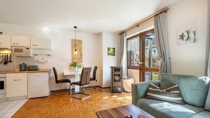 A modern living room with a sofa, a coffee table, a dining area with a table and chairs, a kitchen with a microwave, and a large window with curtains.