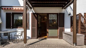 A covered outdoor area with a table and chairs, a wooden bench, and a staircase leading to a door.