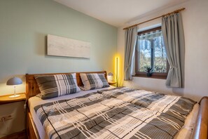 Une chambre à coucher comprenant un lit, des lampes de chevet, une fenêtre avec des rideaux, une œuvre d’art accrochée au mur et une table de chevet.