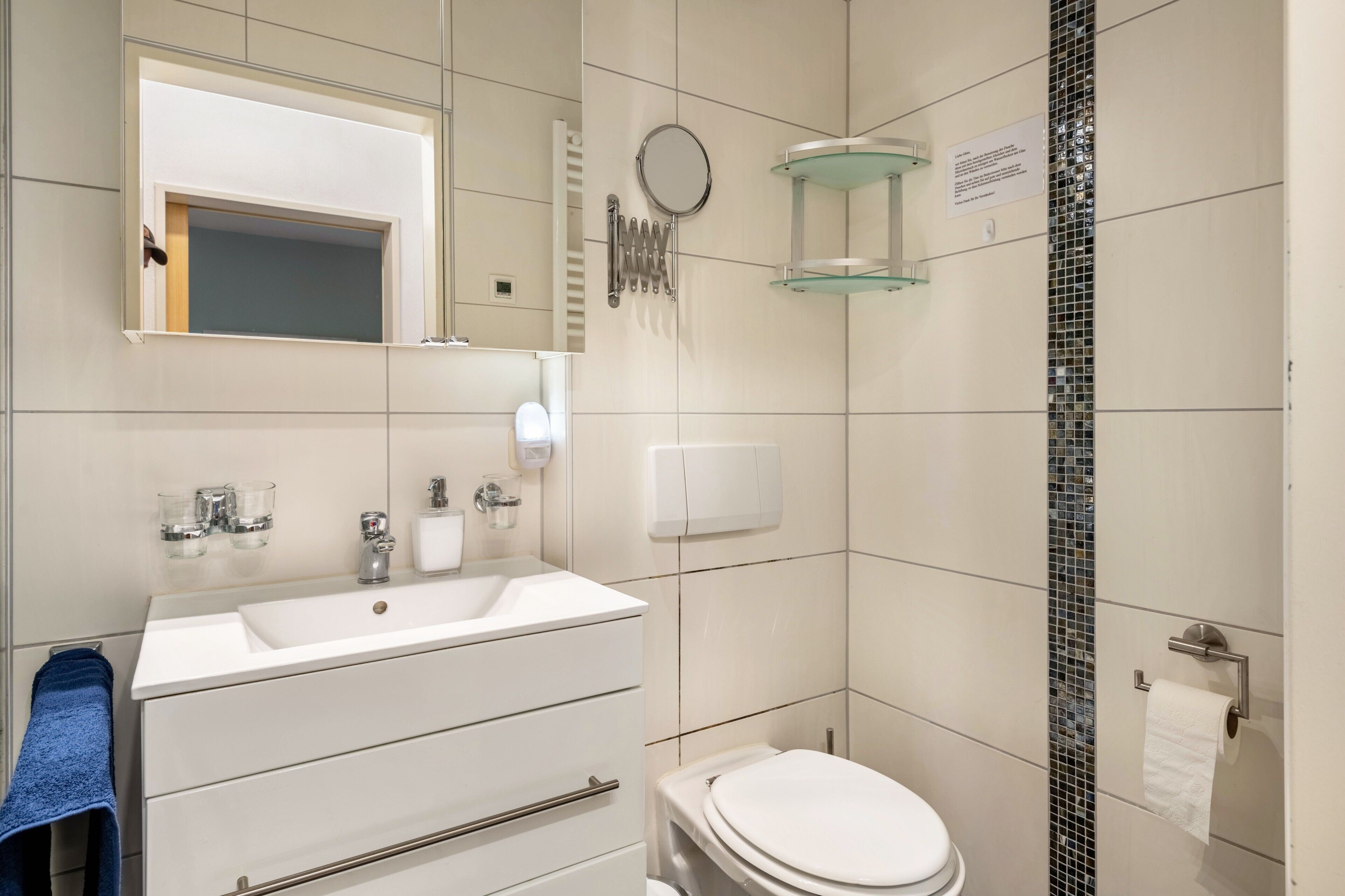 Un baño moderno con lavamanos, espejo y retrete blancos.