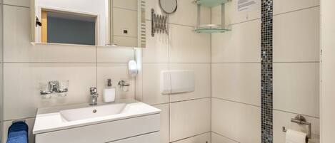 Un baño moderno con lavamanos, espejo y retrete blancos.