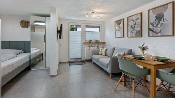 Ein moderner, kompakter Wohnraum mit Bett, Sofa, Esstisch und Bildern an der Wand.