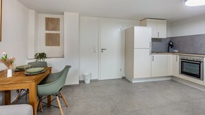 Eine moderne Küche mit weißen Schränken, einem Einbauofen und einem Essbereich mit Holztisch und grünen Stühlen.