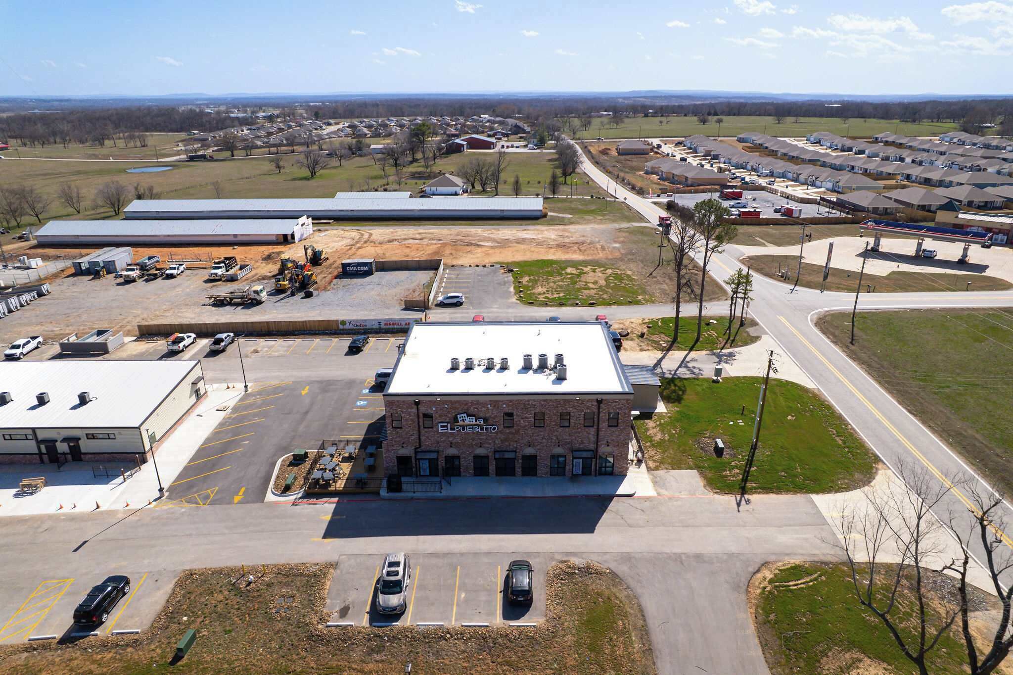 Een bedrijfsgebouw met een parkeerplaats, een tankstation en een groot, open veld op de achtergrond.