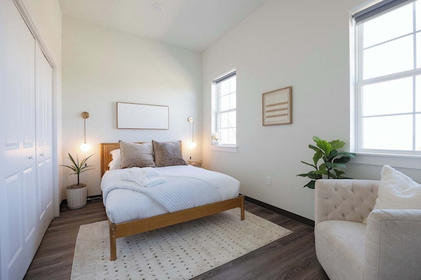 Une chambre à coucher avec un lit, des lampes de chevet, une plante en pot, une chaise et une fenêtre.