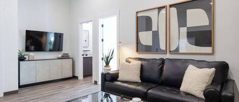Una sala de estar moderna con un sofá de cuero negro, una mesa de centro de vidrio y un televisor de pantalla plana.
