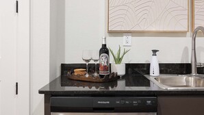 Una cocina con lavavajillas, una botella de vino, copas y una planta en la encimera.