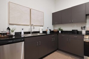 A modern kitchen with dark cabinets, a dishwasher, a sink, and two decorative wall panels. - Navigator - 5 mi to XNA - 15 mi to DT Bentonville (Gentry)