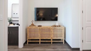A hallway with a TV mounted on the wall, a wicker console table with decorative items, and a dark wooden cabinet.