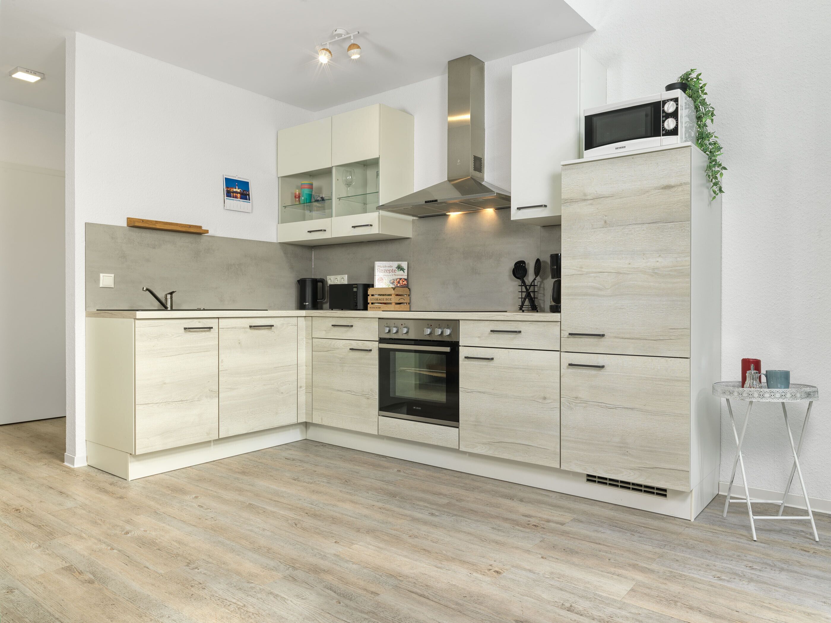 Una cocina moderna con armarios de madera clara, horno integrado y microondas.