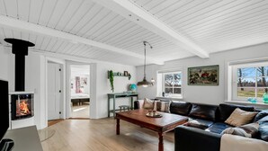 A spacious living room with a fireplace, a dining table, a sofa, and a view of the outdoors through large windows.