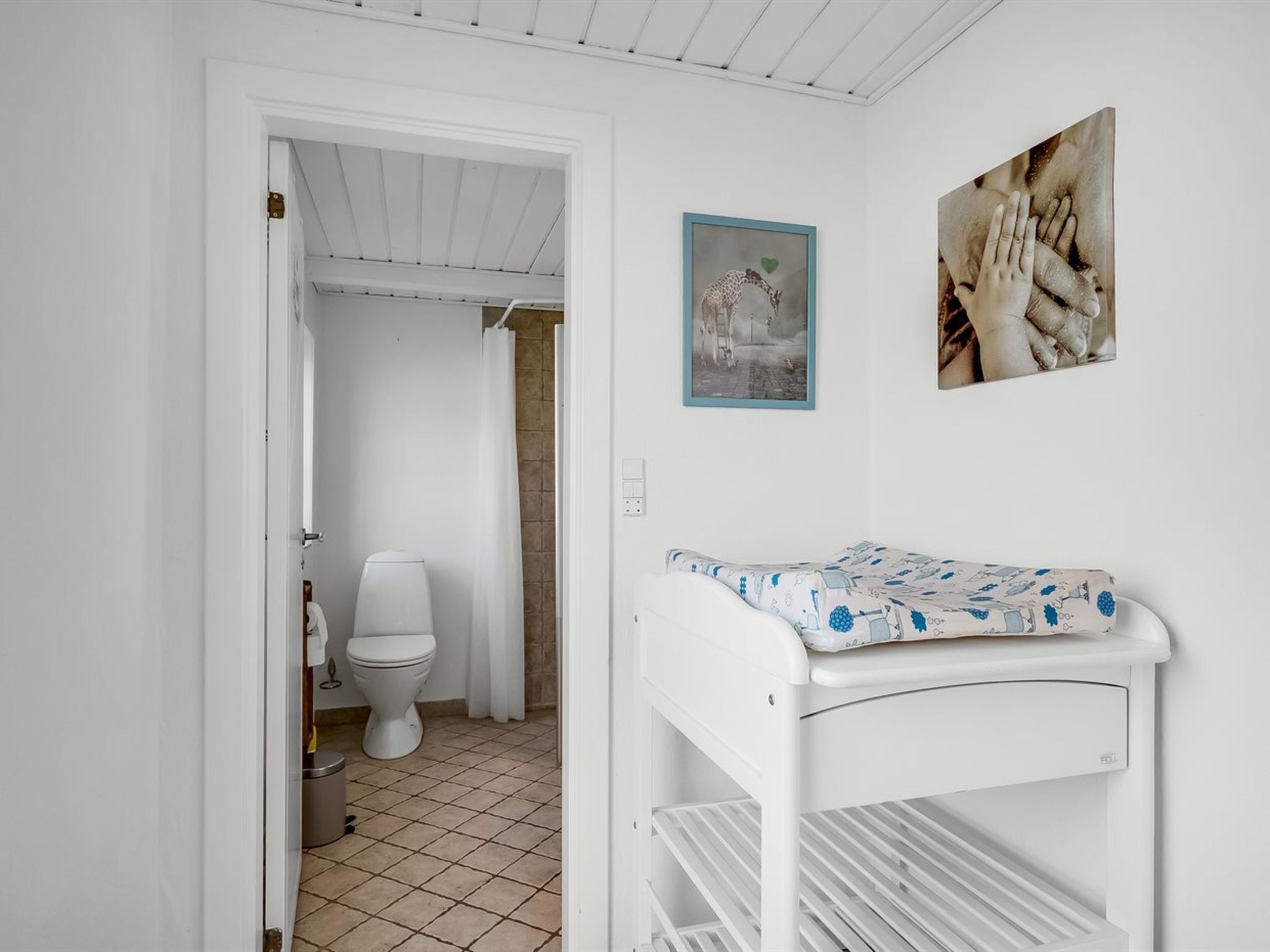 Une pièce blanche avec un lit superposé, des toilettes et une douche. Deux tableaux encadrés sont accrochés au mur.