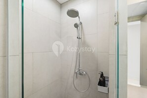 Un baño moderno con ducha envuelta en vidrio, cabezal de ducha de mano y dispensador de jabón.