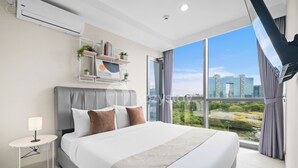 A modern hotel room with a large bed, a bedside table with a lamp, a wall-mounted shelf with decorative items, and a large window offering a city view.