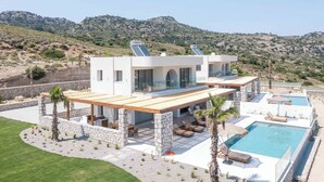 Una villa moderna con piscina, mobiliario exterior y vistas a las colinas circundantes.