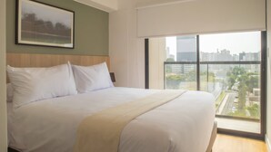 A large bed with white linens, a headboard, and a view of a cityscape through a large window. - w* | Astonishing 1BR w/ Great Deco in San Isidro (Lima)