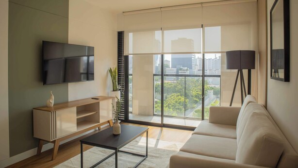 A modern living room with a flat-screen TV, a wooden console table, a beige sofa, and a floor lamp. - w* | Astonishing 1BR w/ Great Deco in San Isidro (Lima)