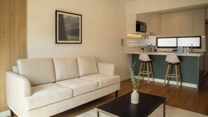 A modern living room with a sofa, a coffee table, and a kitchen area with a bar counter and stools. - w* | Astonishing 1BR w/ Great Deco in San Isidro (Lima)