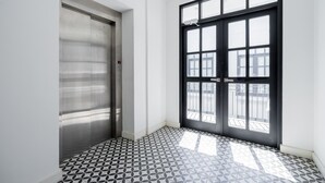 Un pasillo con un ascensor metálico y un amplio ventanal de marco negro que ofrece vistas al exterior.