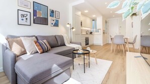 Un salon moderne avec un canapé gris, une petite table ronde et un coin repas comprenant une table blanche et des chaises grises.