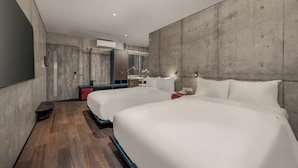 Quarto de hotel moderno com duas camas grandes, piso de madeira, parede de destaque em concreto e um espelho amplo.