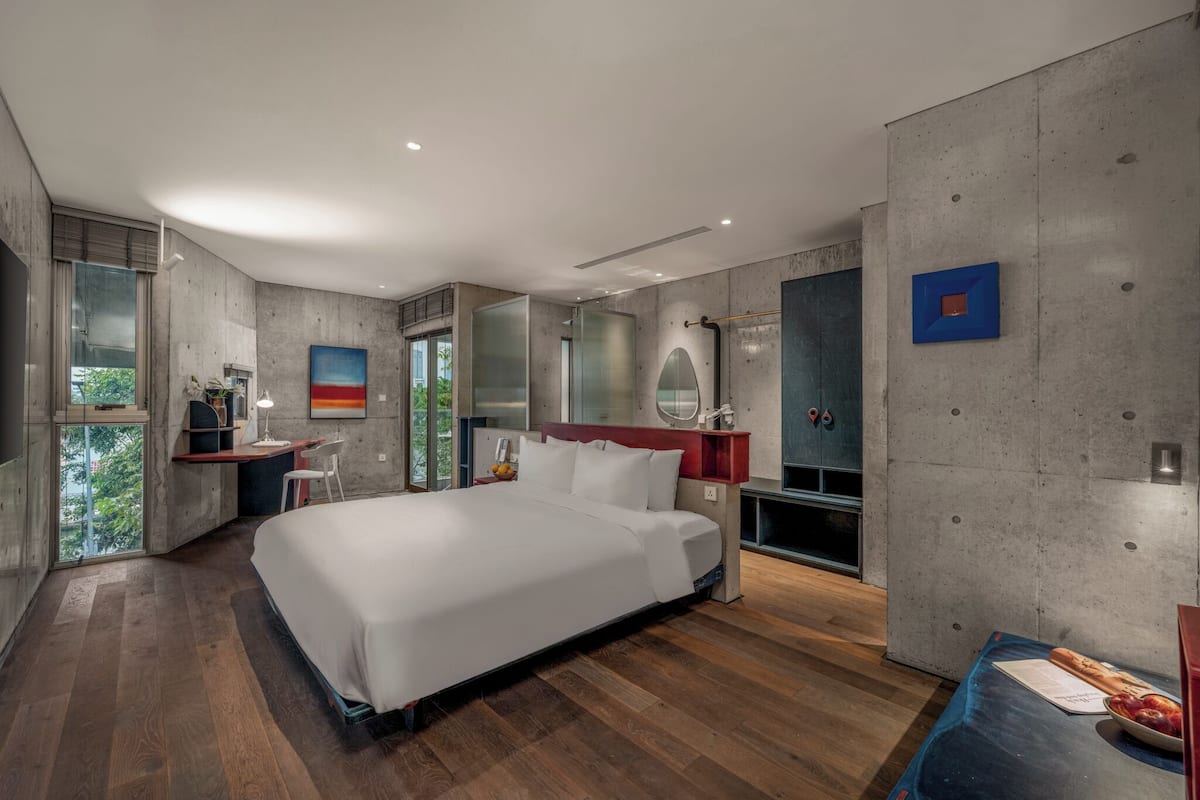A modern bedroom with a large bed, a desk, and a bathroom with a mirror and shower.