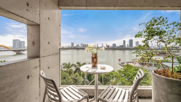 Varanda com duas cadeiras e uma mesa pequena, com vista para um rio e o horizonte urbano.