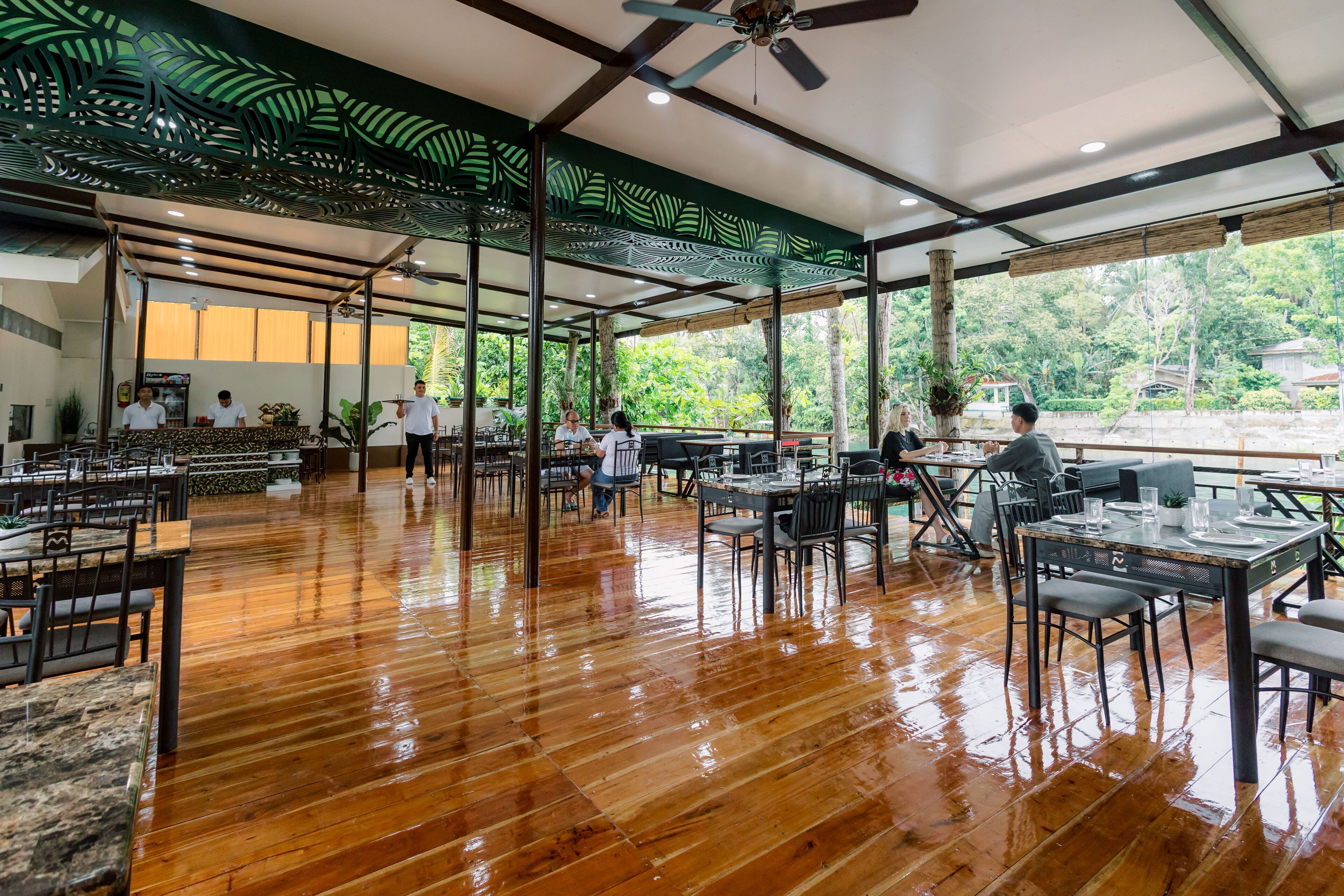 A spacious restaurant with wooden flooring, large windows, and a ceiling fan.