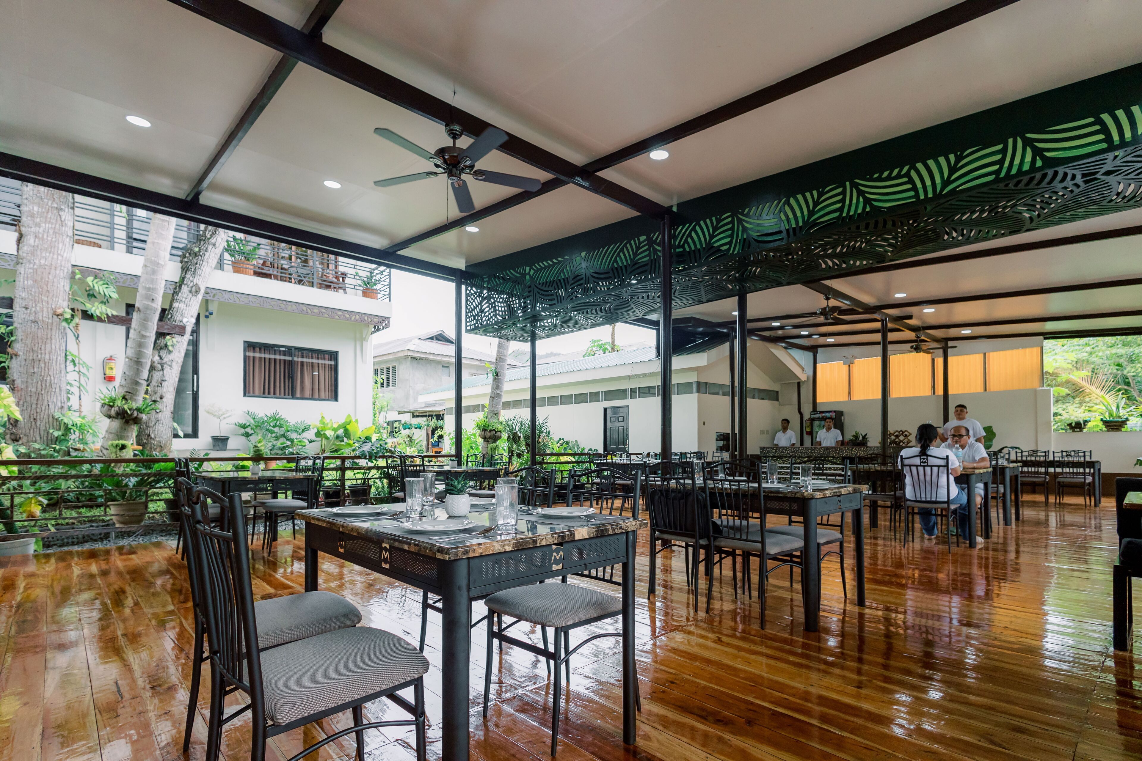 An indoor dining area with wooden flooring, tables with chairs, ceiling fans, and a view of the outside.