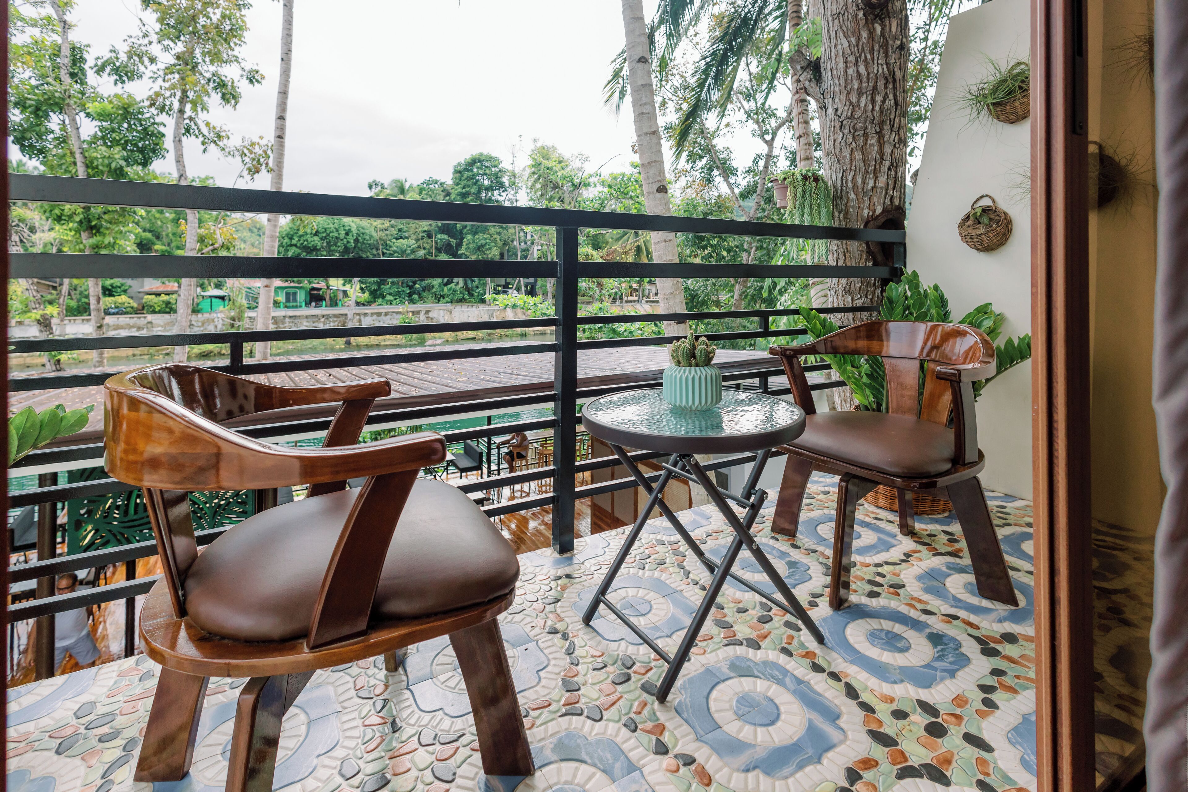 A balcony with two wooden chairs and a small table, surrounded by a tiled floor with a geometric pattern.