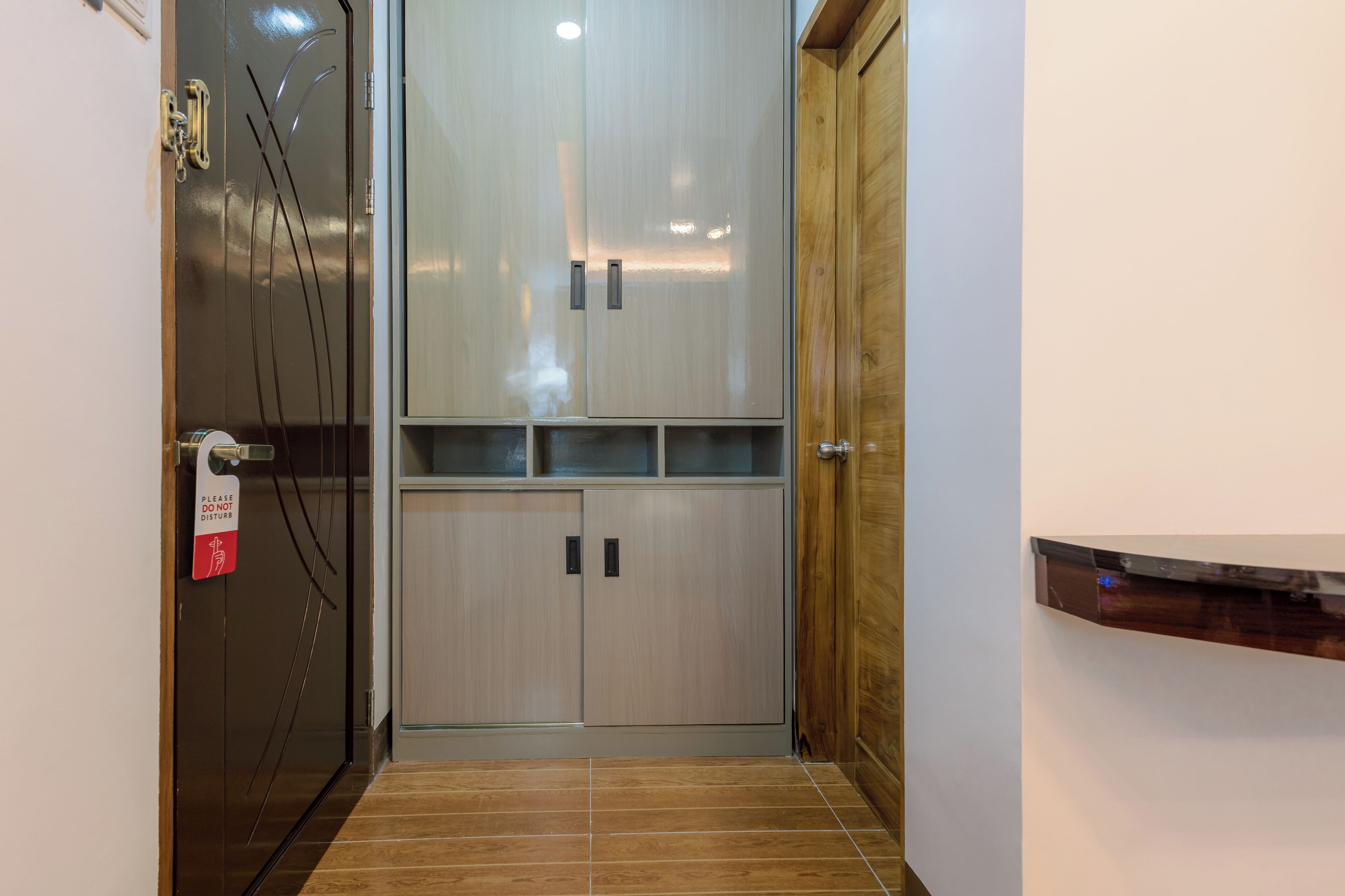 Un couloir étroit avec une porte d’ascenseur en métal, une porte en bois et un sol carrelé.