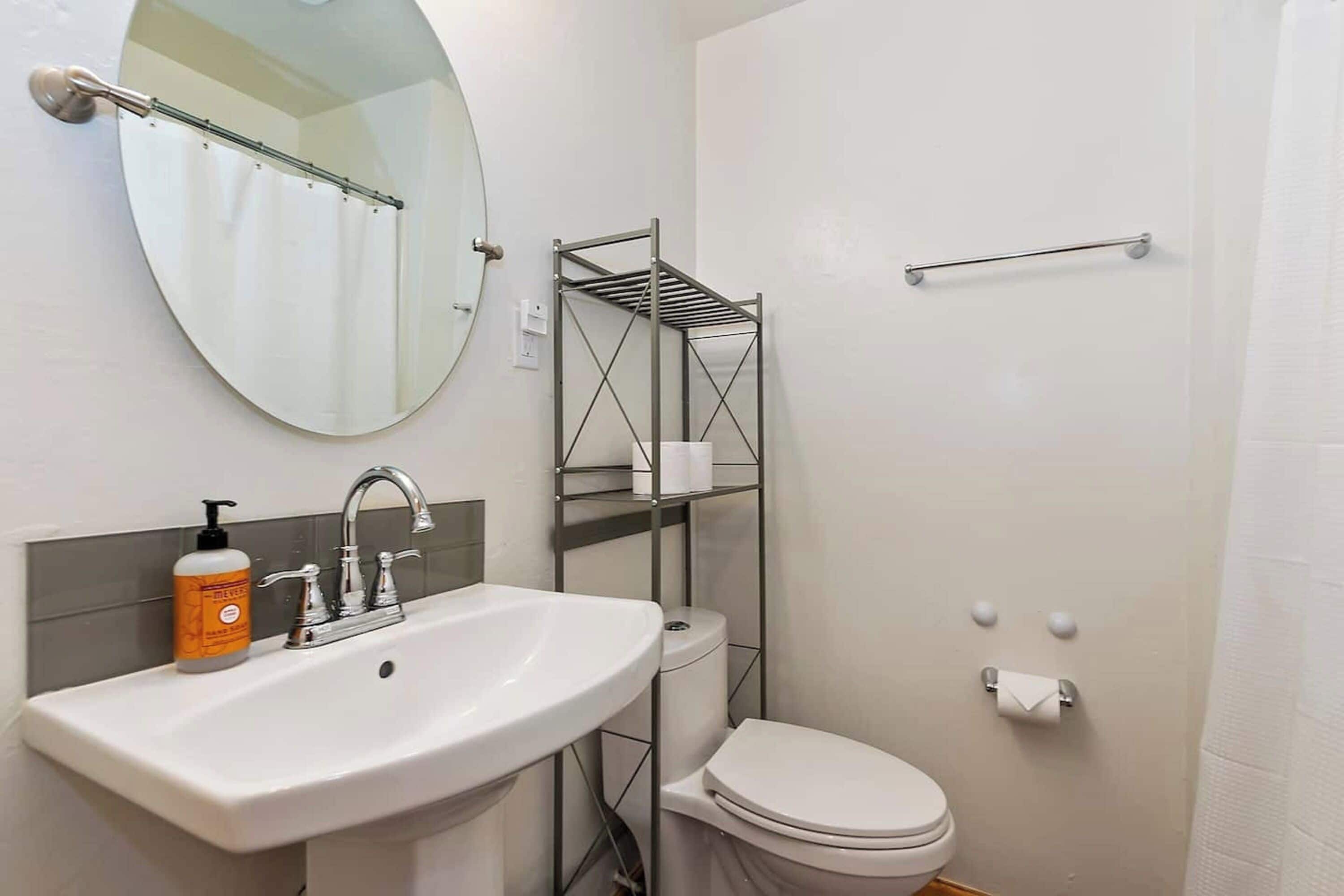 Une salle de bain avec un lavabo blanc, un miroir, des toilettes et une étagère en métal.