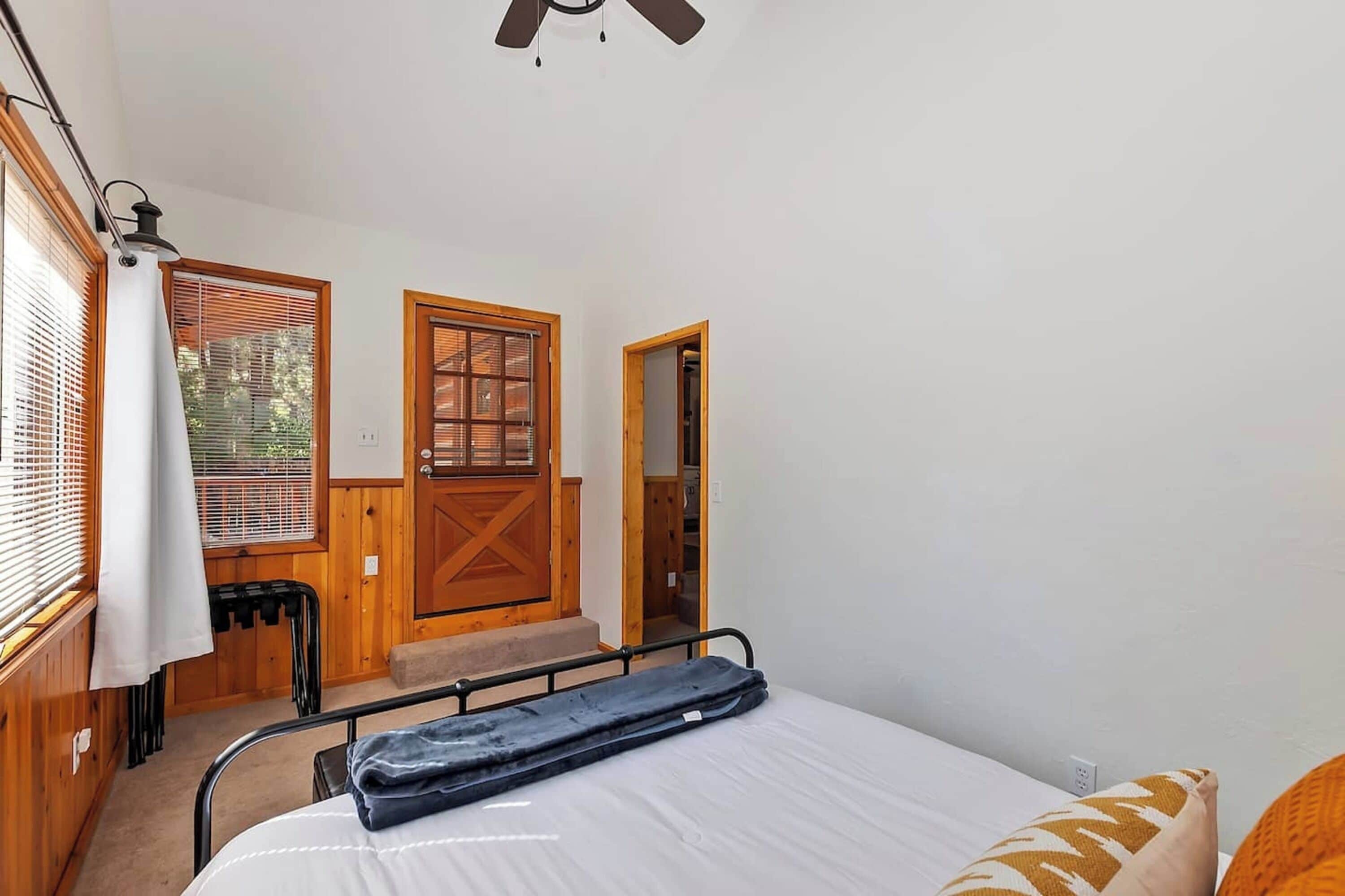 A bedroom with a bed, a wooden door, a window with blinds, and a ceiling fan.