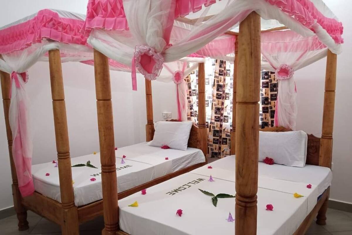 A room with two wooden four-poster beds, each with a white mattress and pink decorative elements.