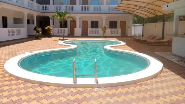 A swimming pool with a white border and a ladder, surrounded by a tiled patio. - Kings Holiday resort watamu (Watamu)