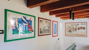 Een galerij met ingelijste kunstwerken aan de muur, houten balken in het plafond en een trap met glazen leuningen.