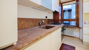 Een keuken met een granieten aanrecht, een roestvrijstalen spoelbak en een raam met uitzicht op buiten.