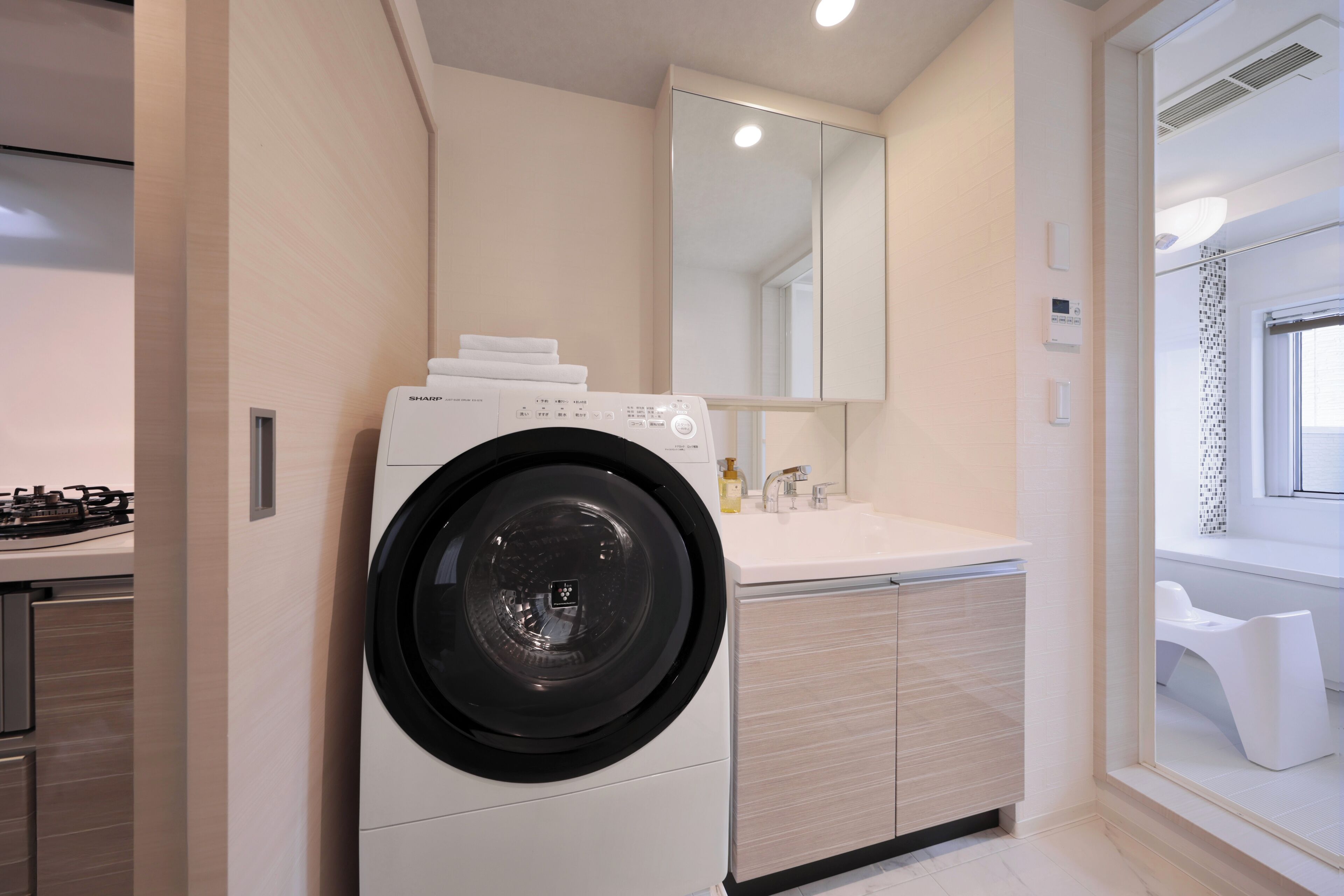 A modern laundry room with a front-loading washing machine, a sink, and a mirror above the counter.