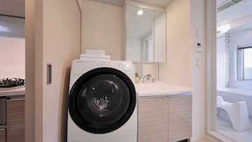 A modern laundry room with a front-loading washing machine, a sink, and a mirror above the counter.