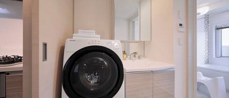 A modern laundry room with a front-loading washing machine, a sink, and a mirror above the counter.