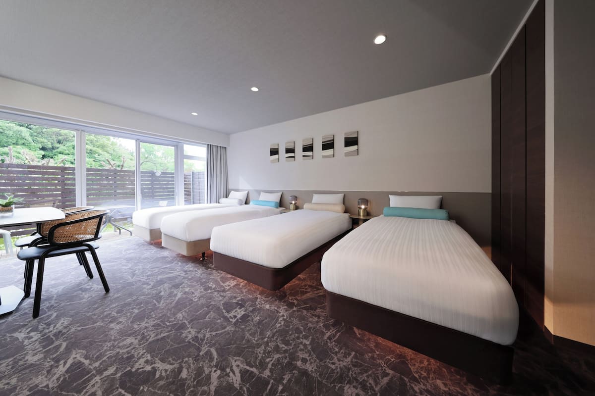 Une chambre d’hôtel avec trois lits, une table à manger et une vue sur la verdure environnante.