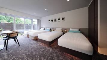 A hotel room with three beds, a dining table, and a view of greenery outside.