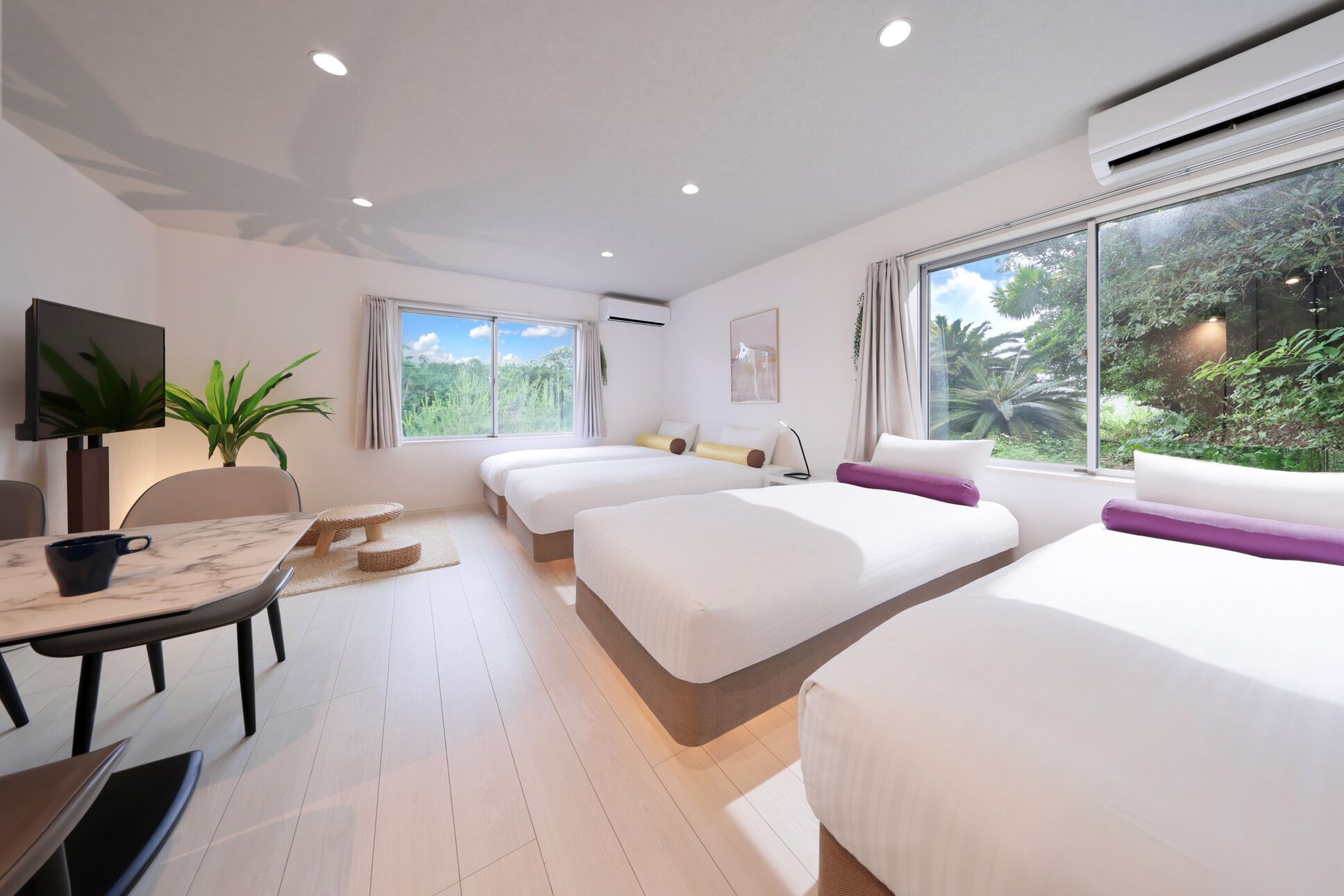 A hotel room with two beds, a TV, a desk with a chair, a coffee cup, and a window with a view of greenery.